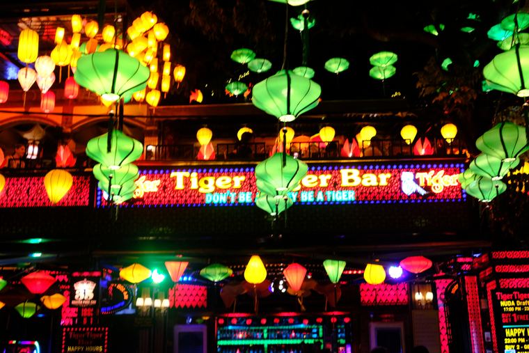 Silk lanterns strung above a neon bar front at night